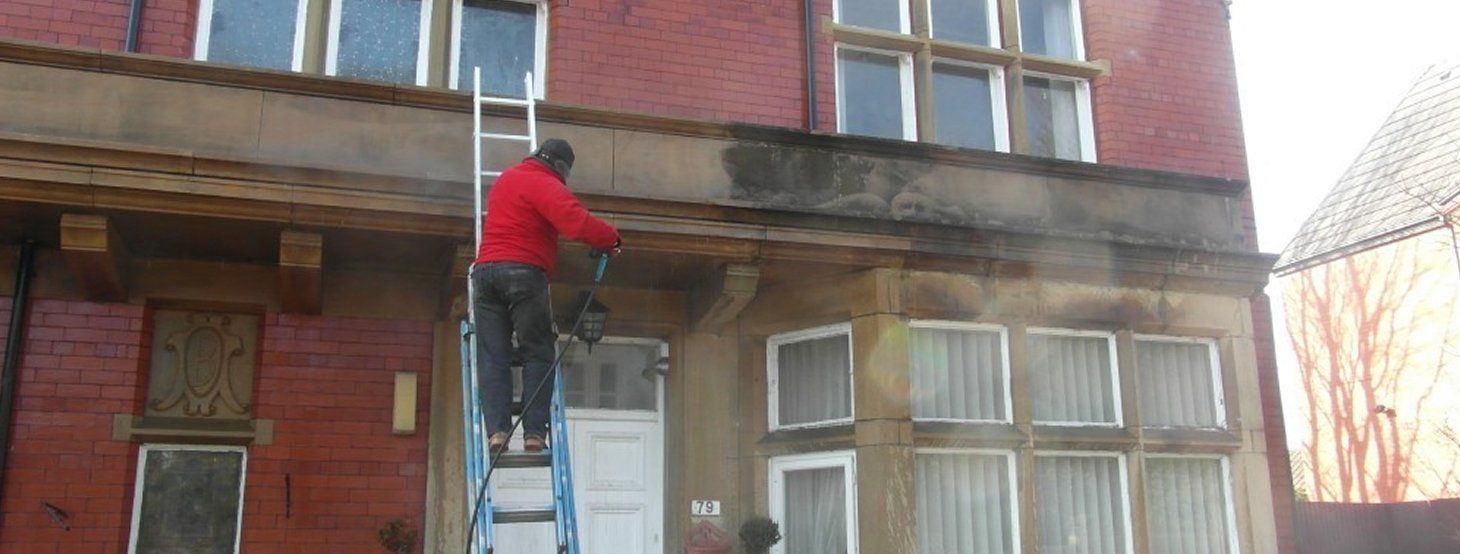 A man is standing on a ladder cleaning a brick building.