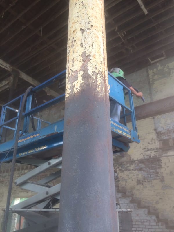 A man in a green hard hat is standing on a blue scissor lift