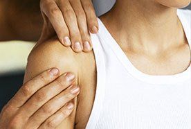 A therapist massaging the shoulder of a lady in a white vest