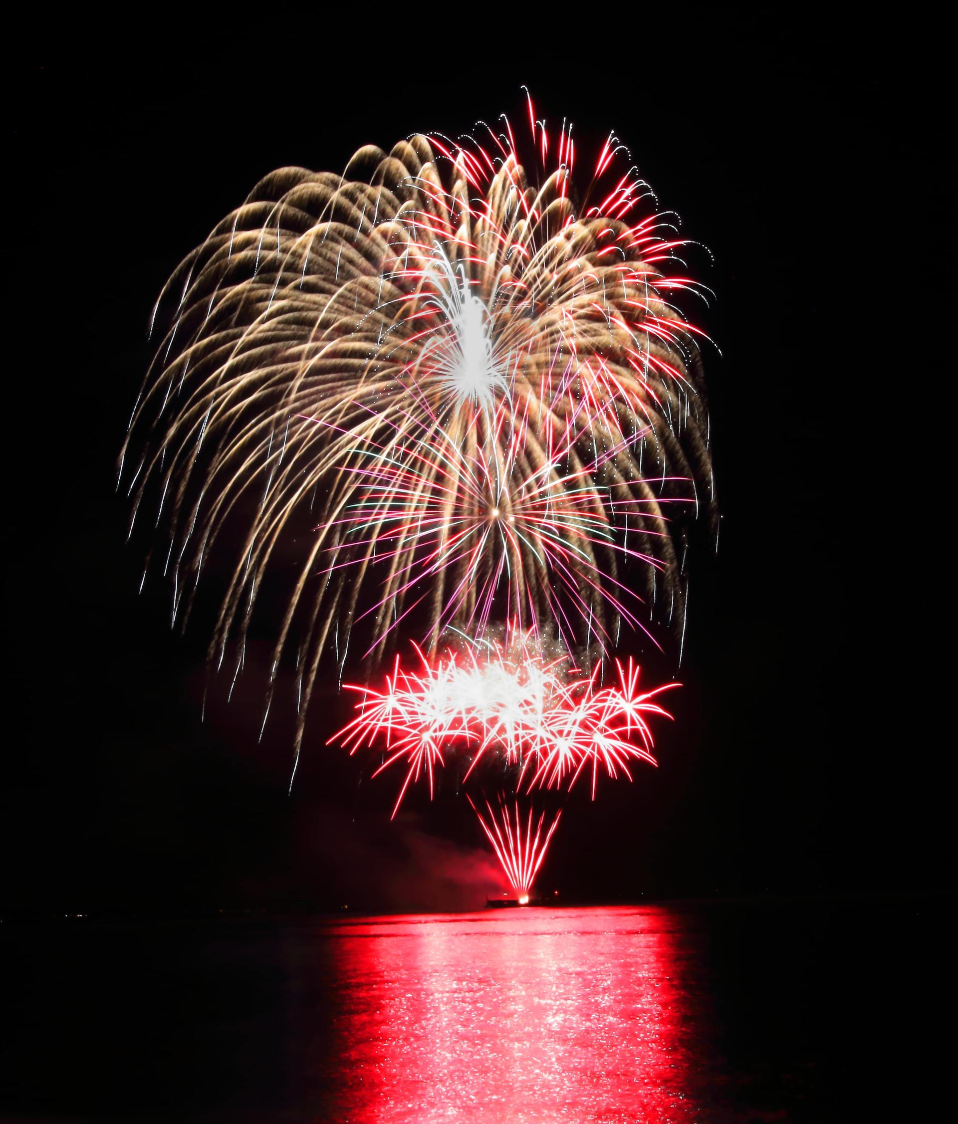 A fireworks display over a body of water at night.