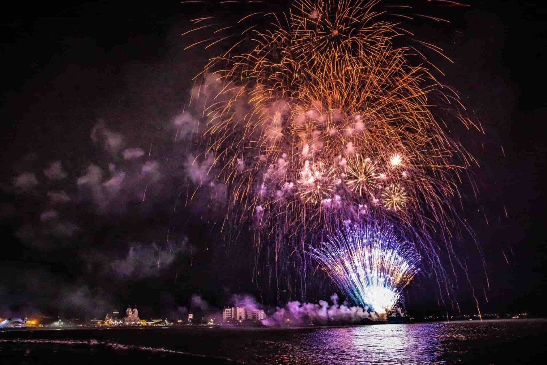 A fireworks display over a body of water at night.