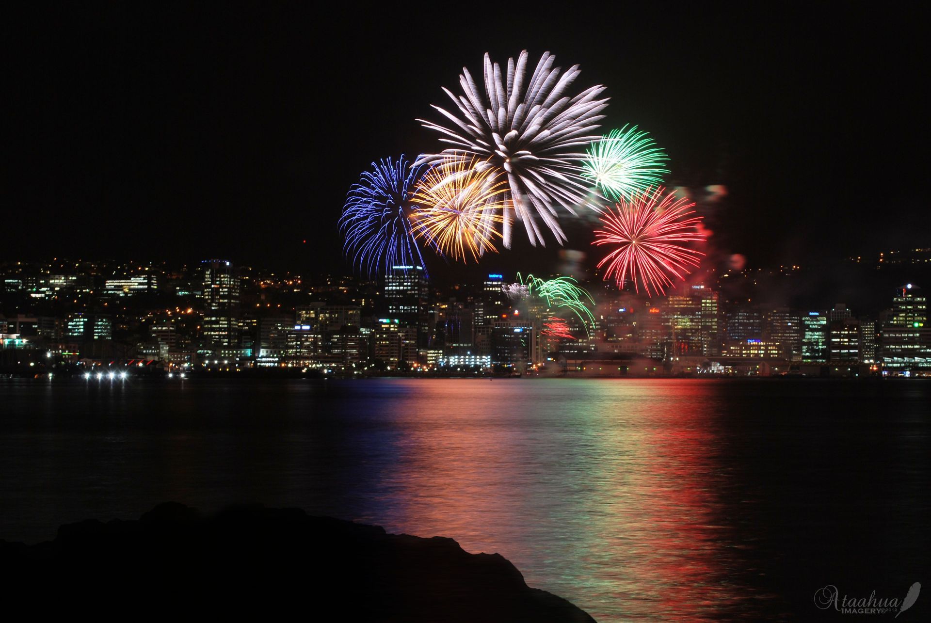 A fireworks display over a body of water with a city in the background