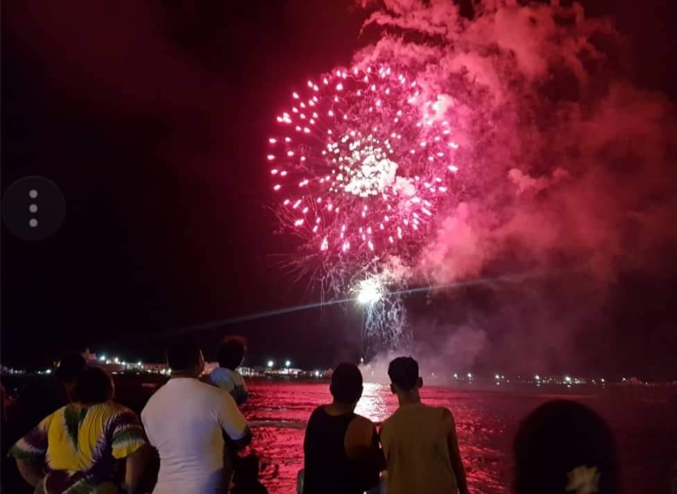 A group of people are watching fireworks over the ocean.