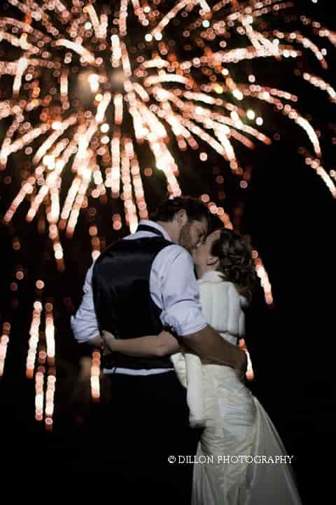 A bride and groom kissing in front of fireworks