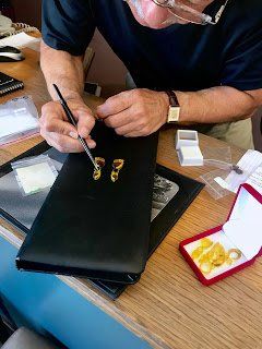 A man is sitting at a table working on a piece of jewelry.
