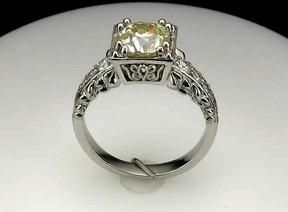 A white gold ring with a yellow diamond in the center is sitting on a white surface.