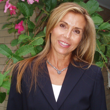 A woman wearing a black jacket and a necklace smiles for the camera