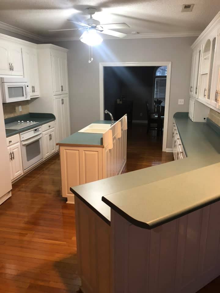 A kitchen with white cabinets , green counter tops , a sink and a ceiling fan.