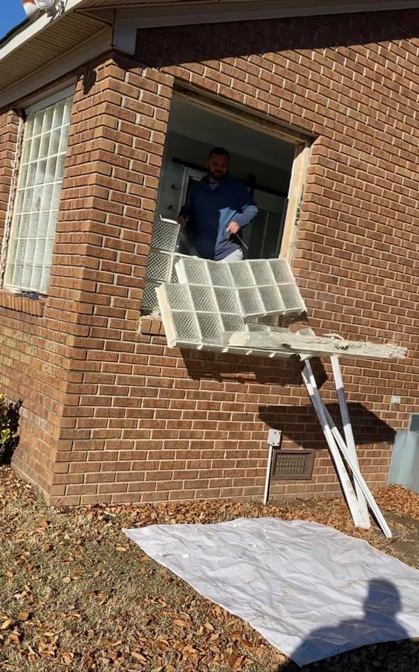 A man is standing in a window of a brick house.
