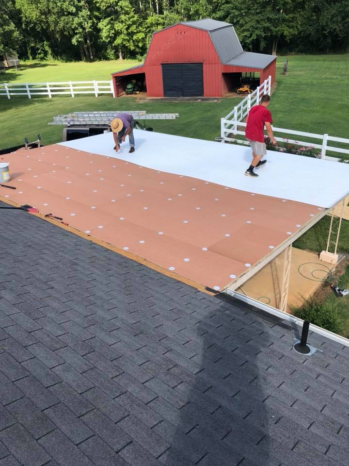 Two men are working on a roof with a barn in the background.