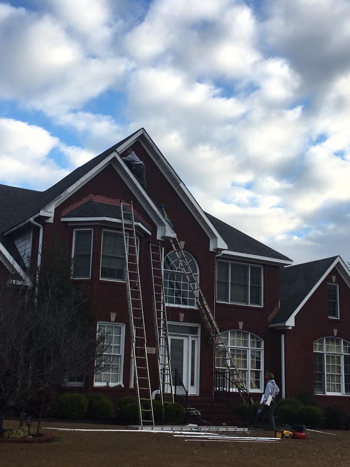 A large red brick house is being painted by a man on a ladder