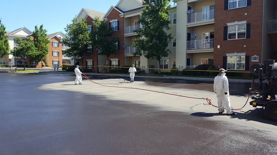 A group of people are spraying asphalt in a parking lot in front of a building.