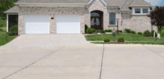 A house with two garage doors and a concrete driveway in front of it.
