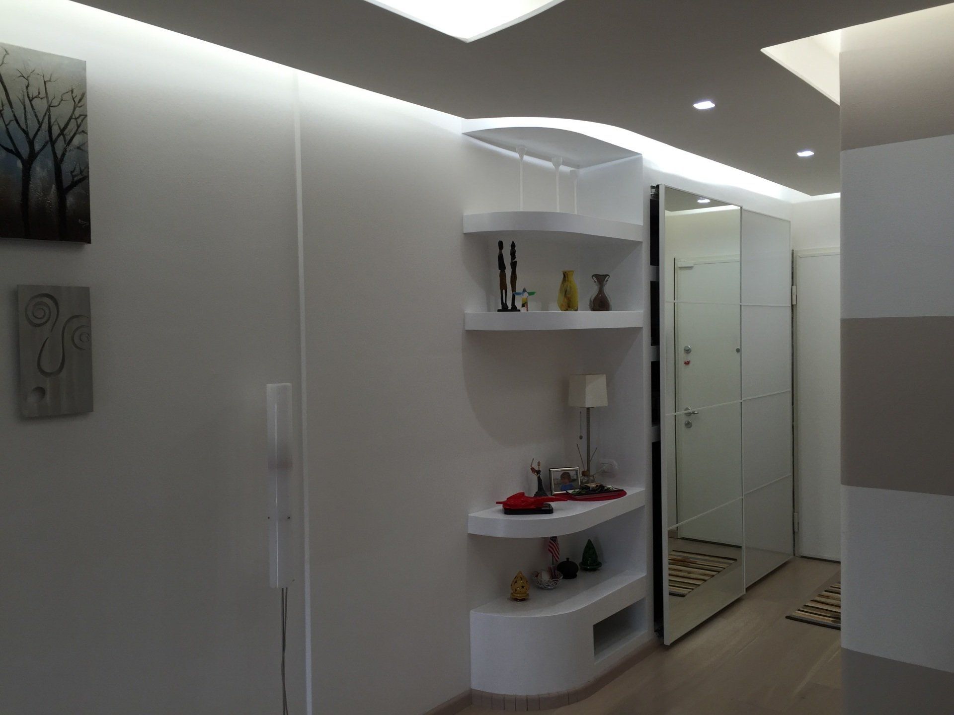 Corridoio bianco con mensole integrate che espongono decorazioni, un grande specchio e illuminazione da incasso.