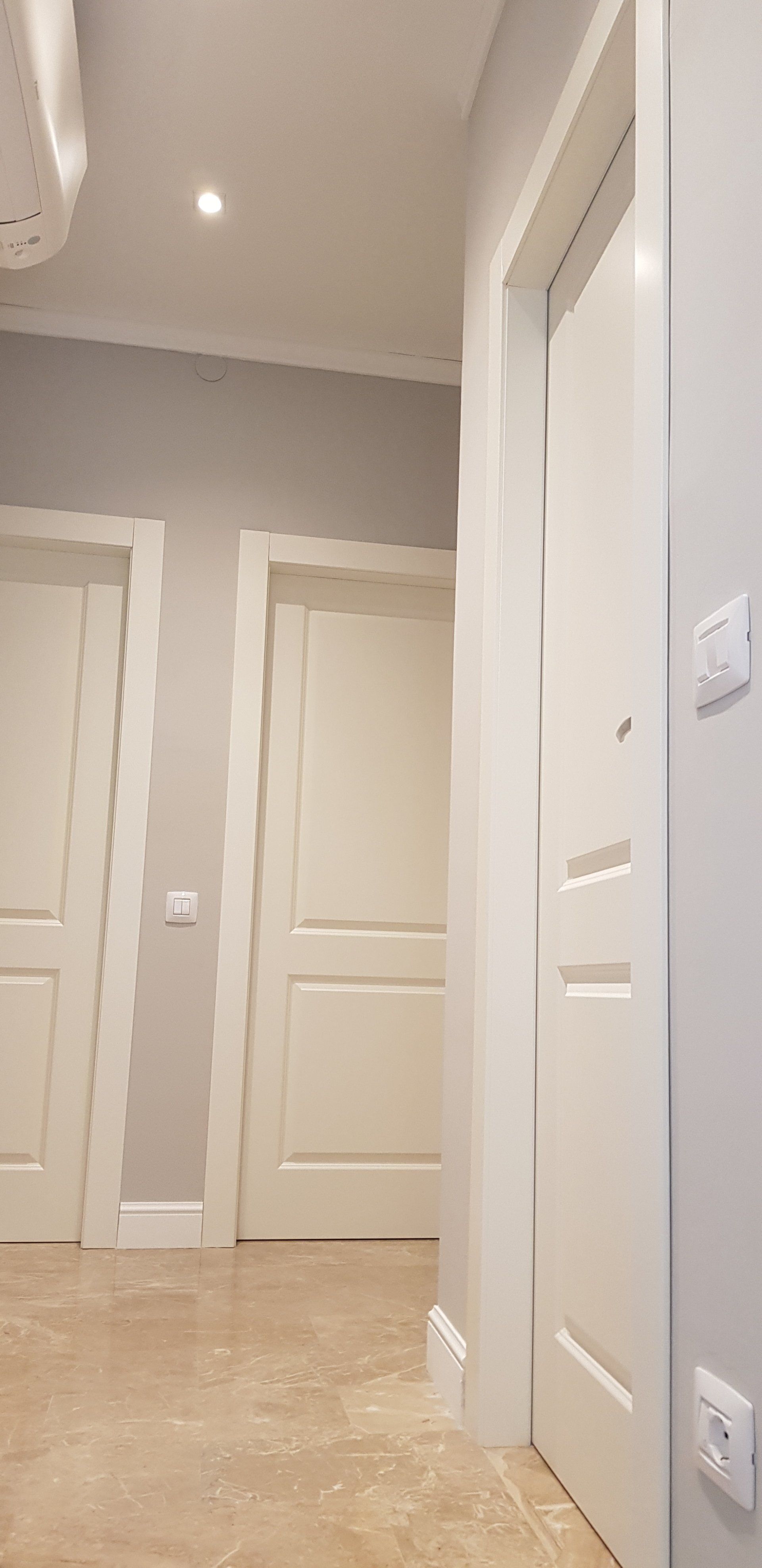 Corridoio con porte bianche, pareti e pavimento di colore chiaro e una lampada a soffitto.