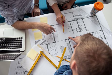 A group of people are sitting around a table looking at a blueprint of a house.