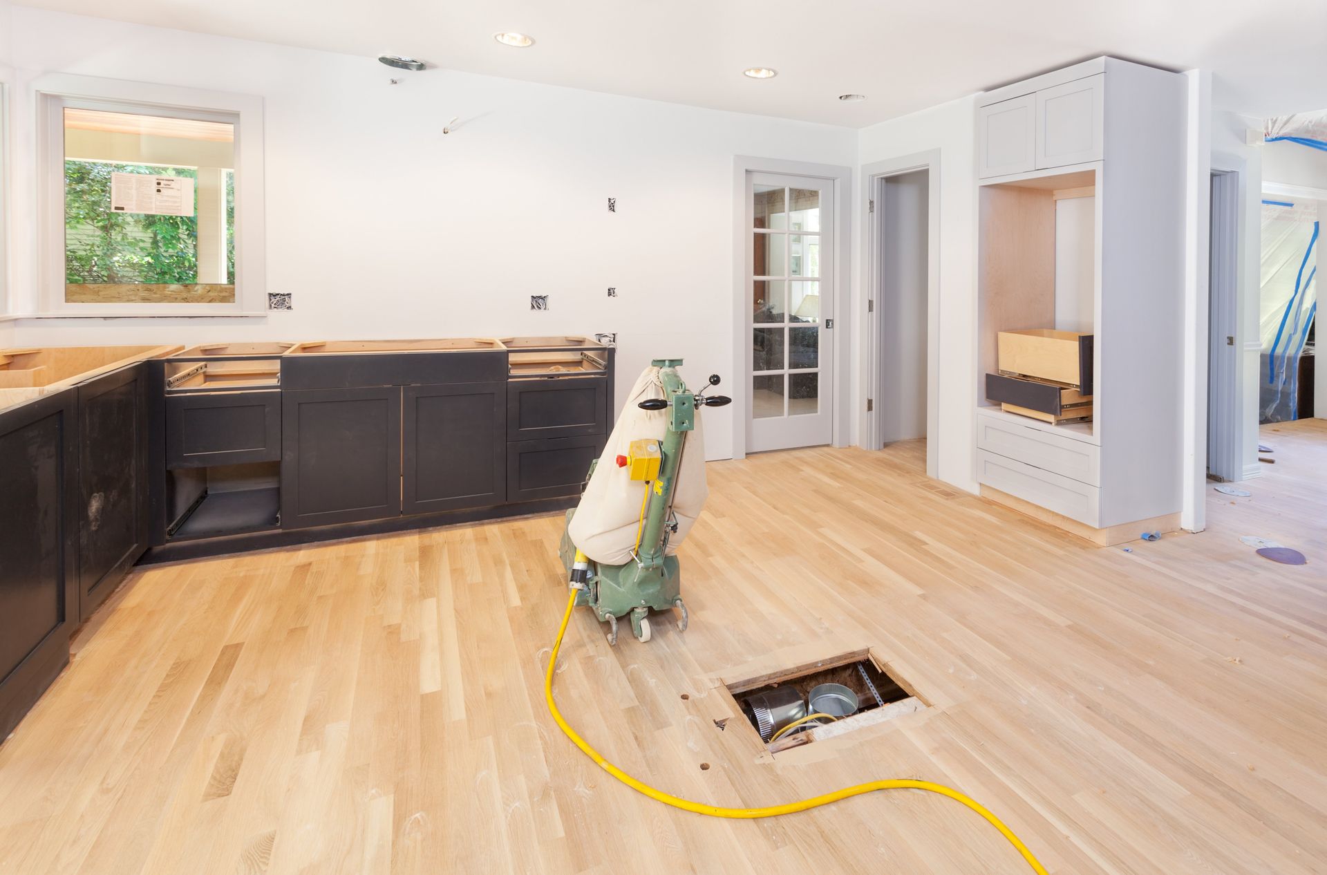 A wooden floor is being sanded in a kitchen.