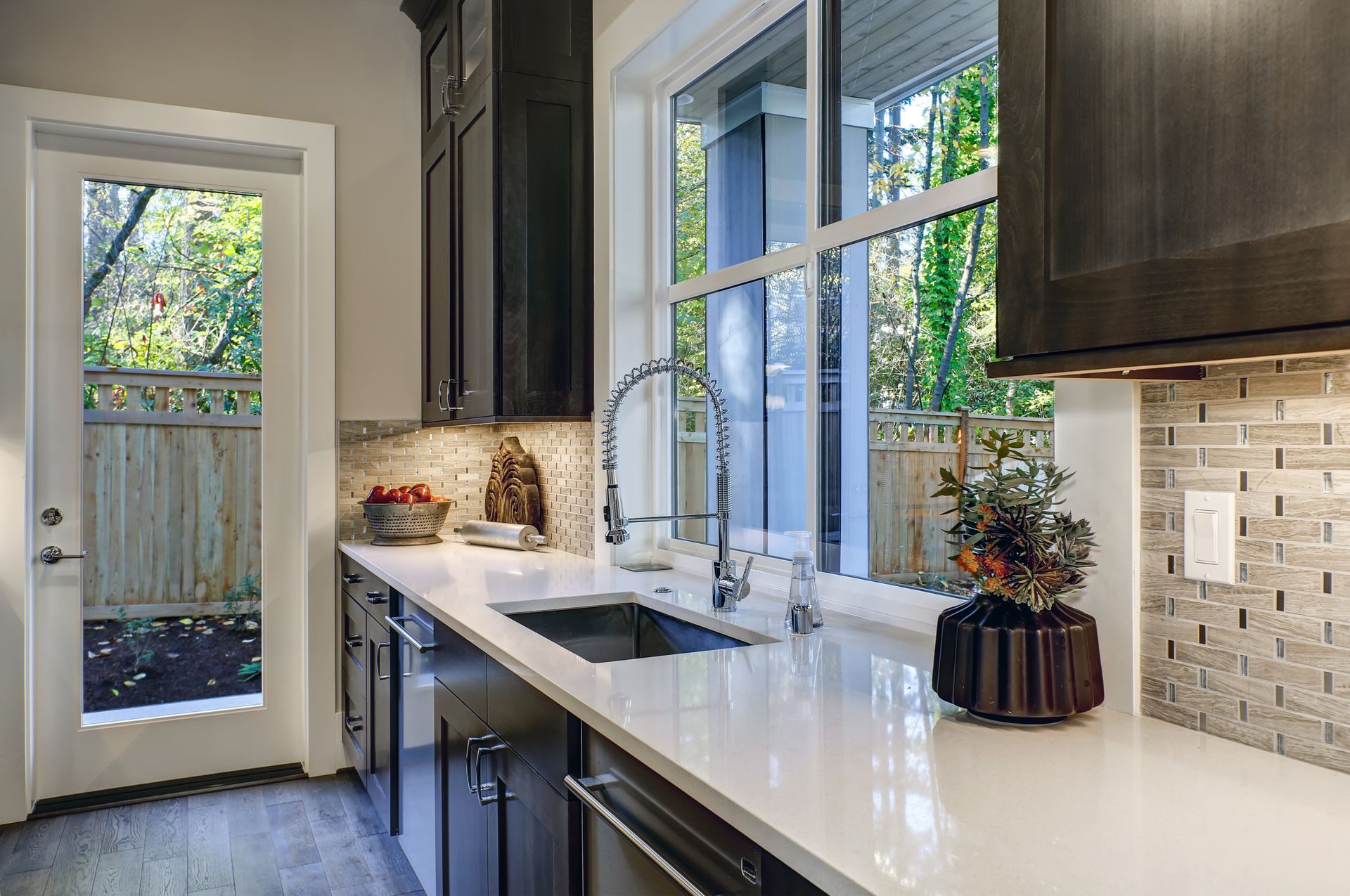 A kitchen with a sink and a window with a view of the backyard.
