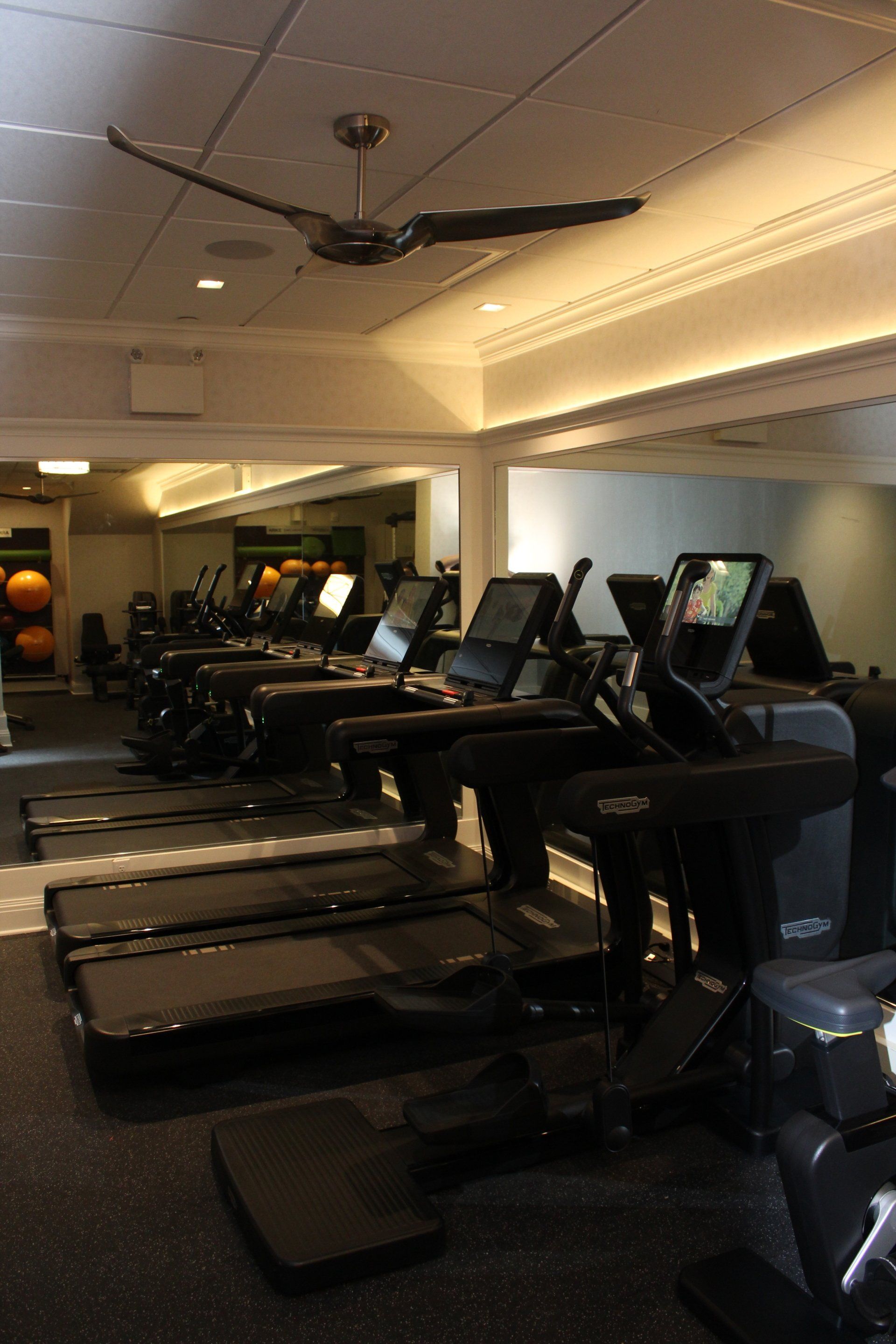 Fitness center with treadmills featuring digital screens lined up against mirrored walls.