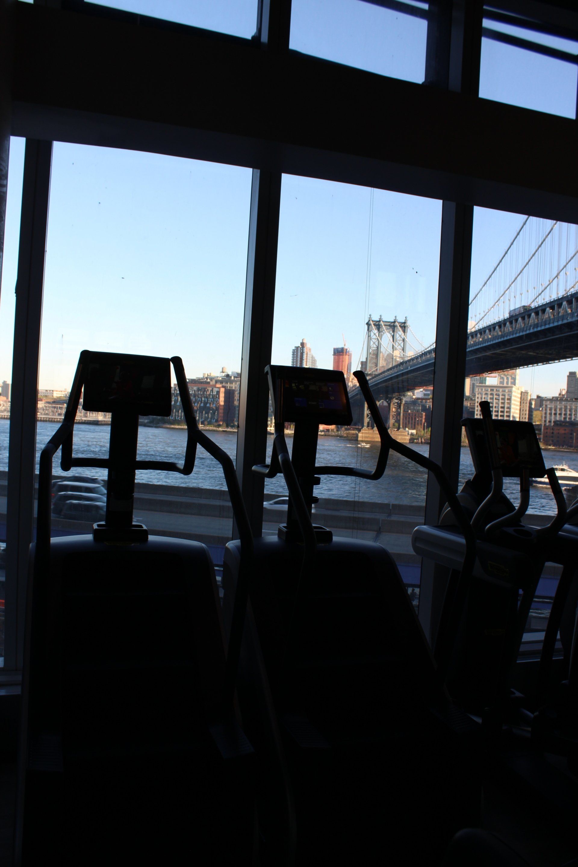 Exercise bikes facing East River with bridge and city views through large windows.