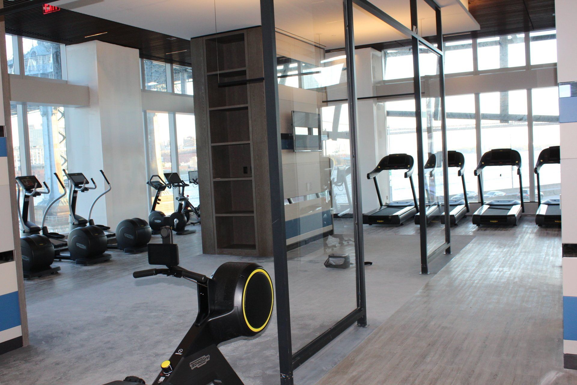 Fitness room with cardio and strength machines, bright windows, and open floor plan.