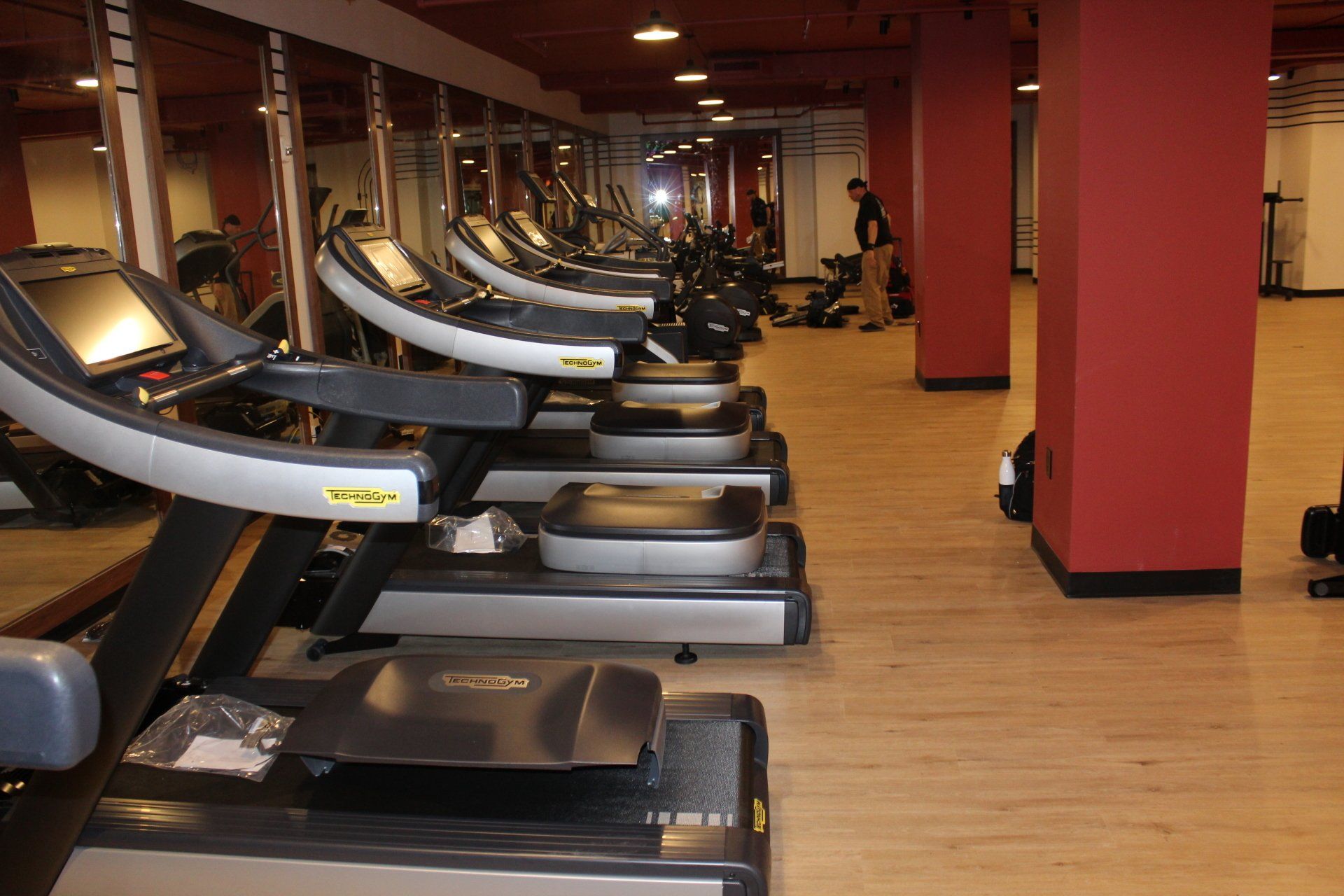 Large row of treadmills in a spacious gym with red walls.