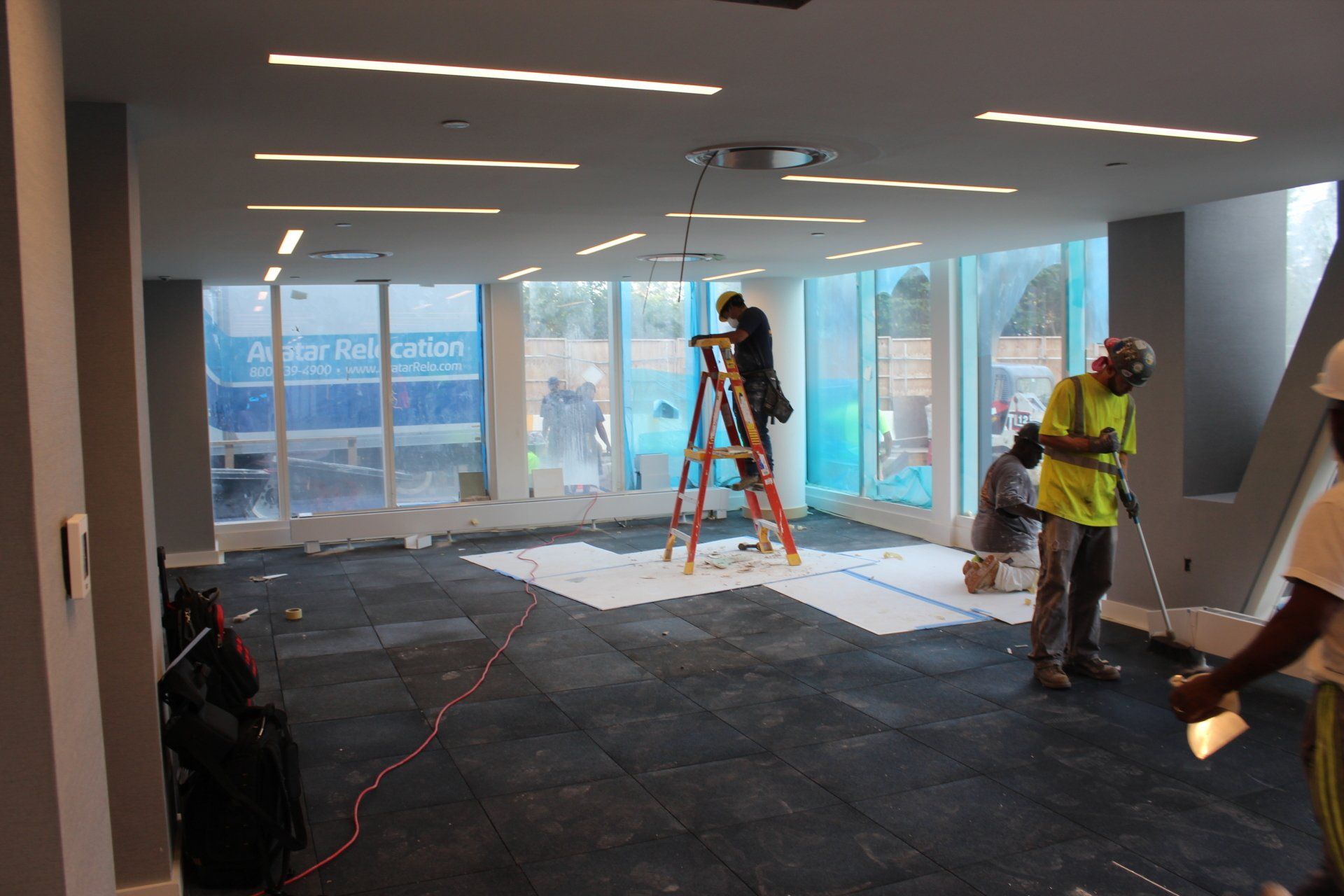Workers installing flooring and lights during Quay Tower renovation project with tools and ladder.
