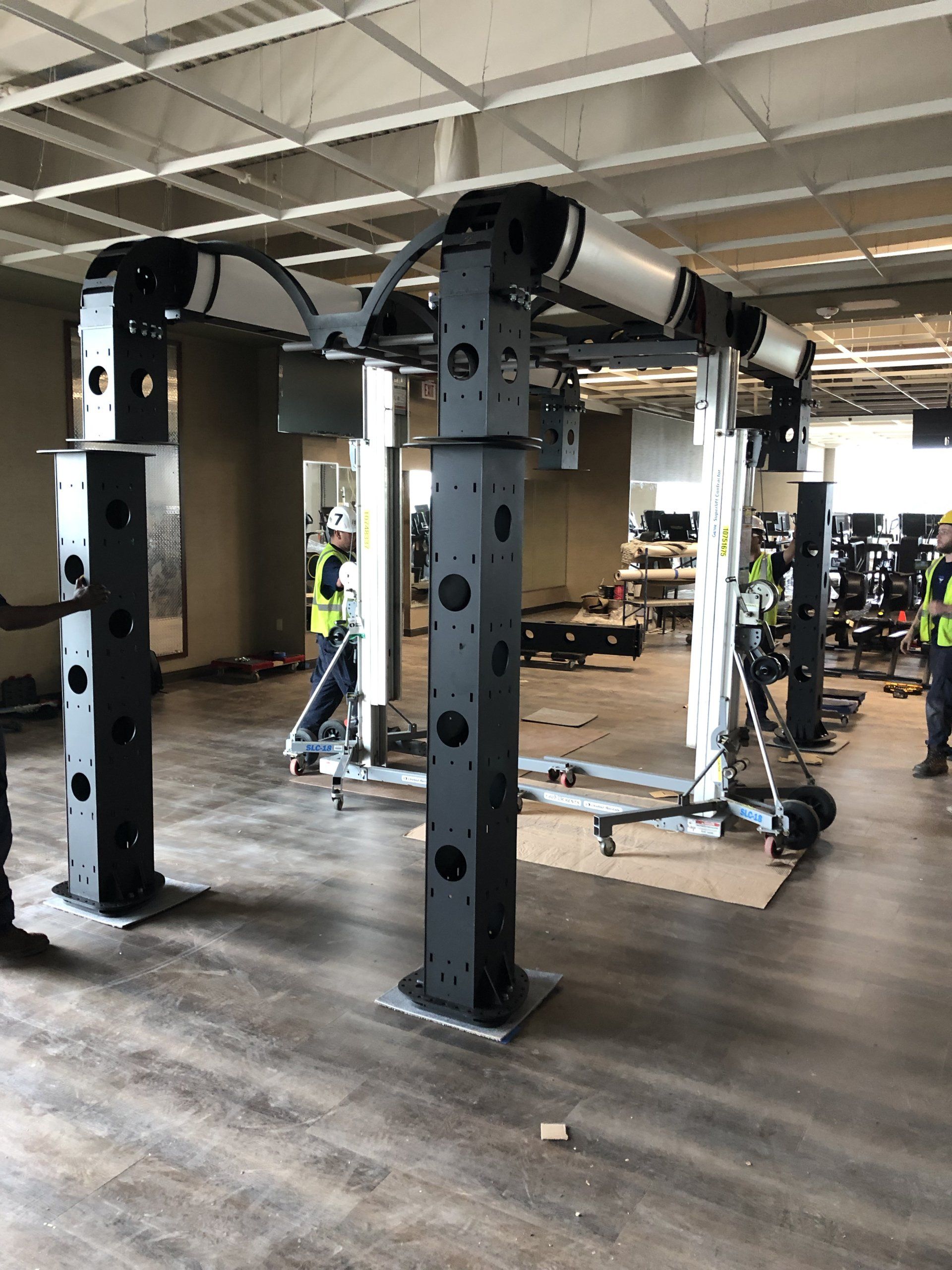 Gym installation in progress with strength training equipment and workers in safety vests.