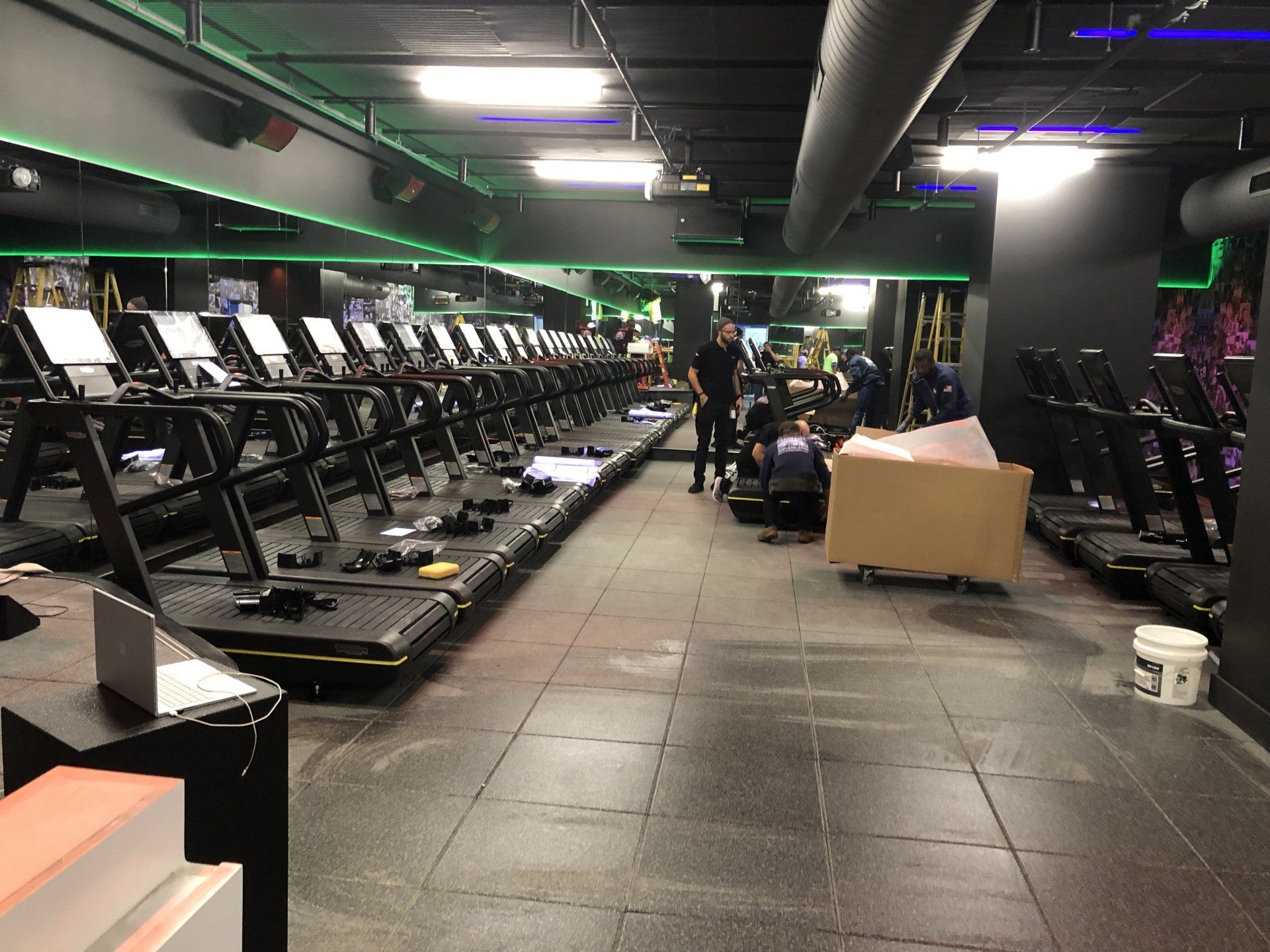 Row of treadmills in a modern gym with black flooring and neon green lighting accents.
