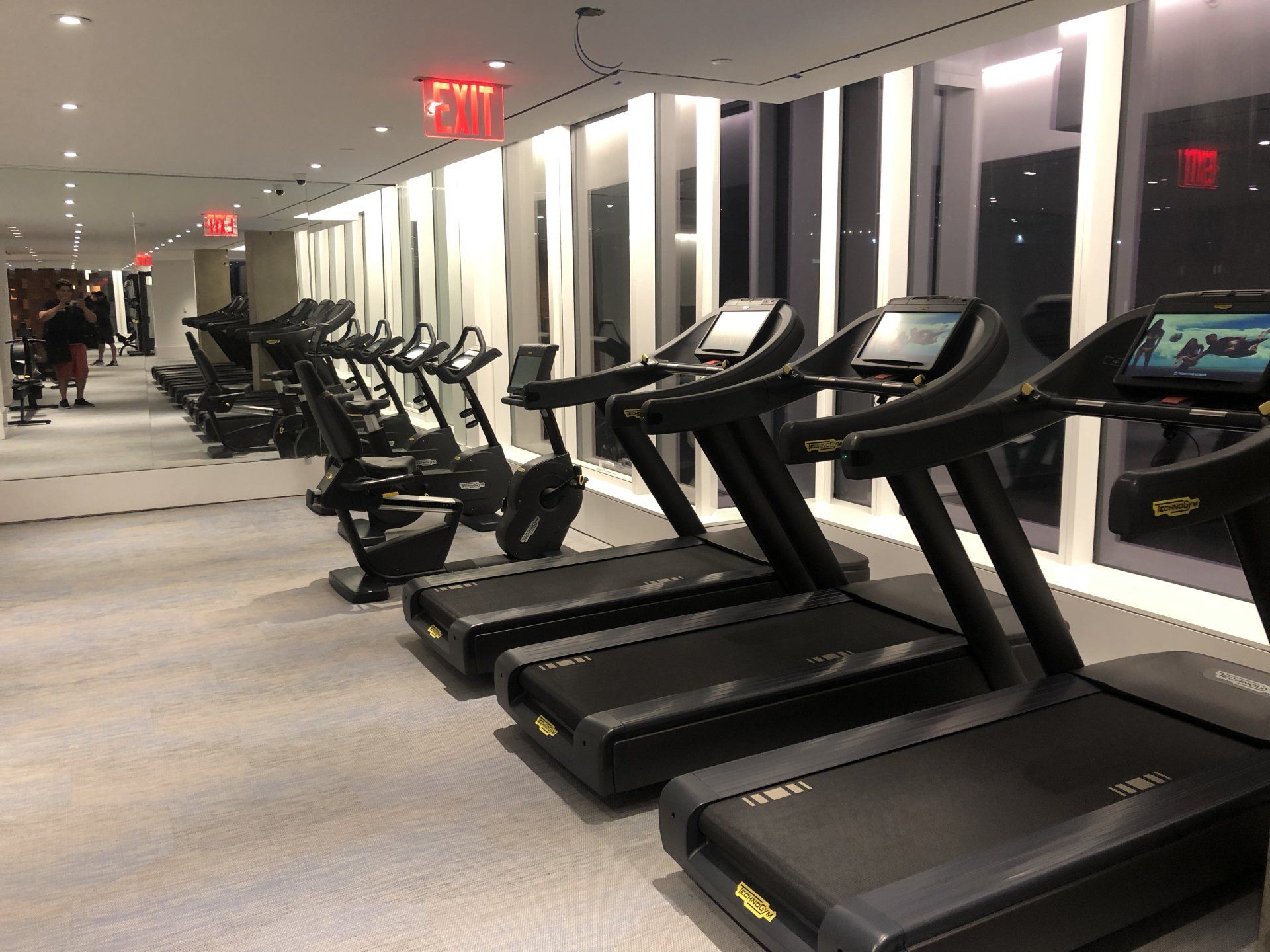 Black treadmills lined up in a sleek modern gym with mirrors and lighting