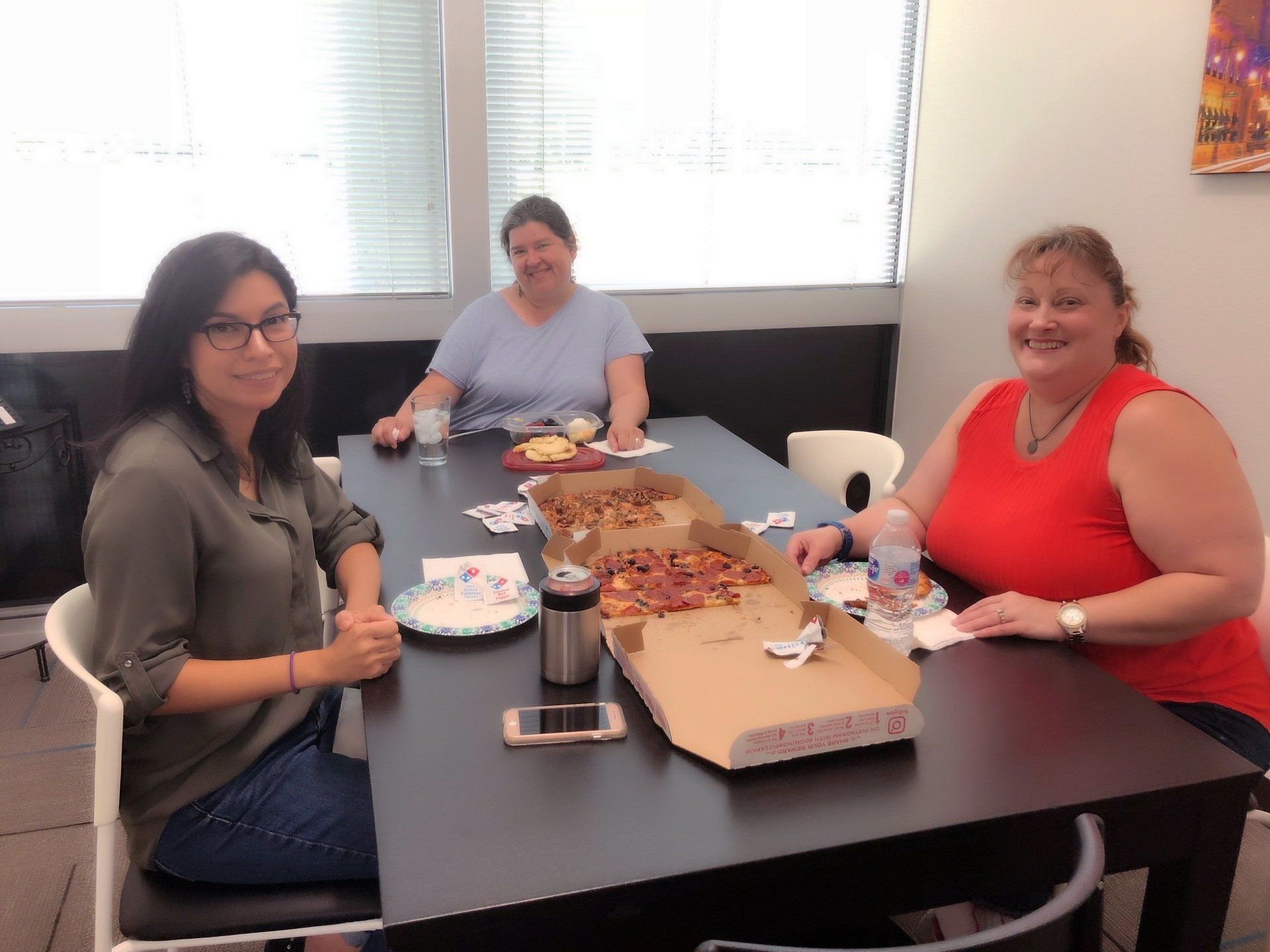Three women are sitting at a table eating pizza