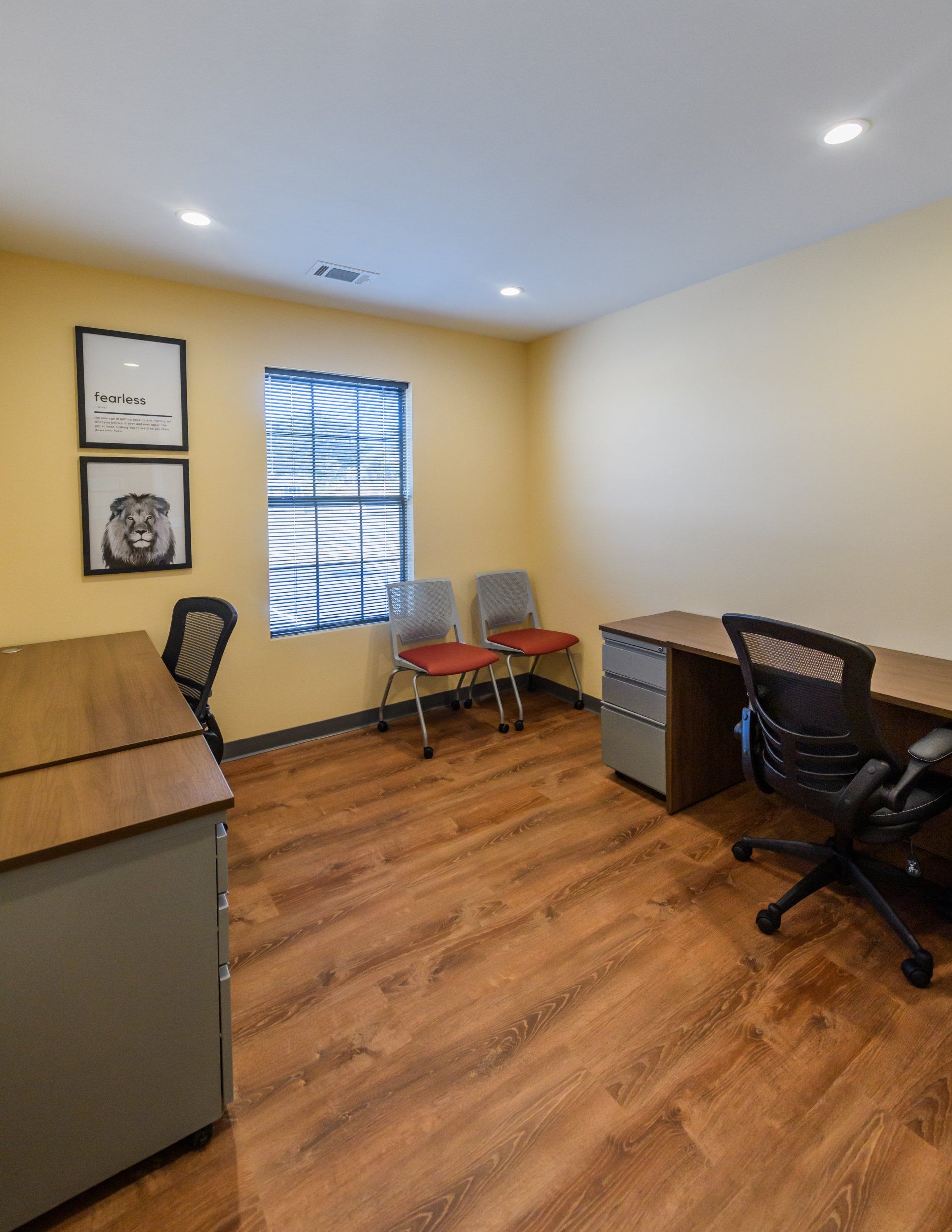 A small office with a desk , chairs and a window.