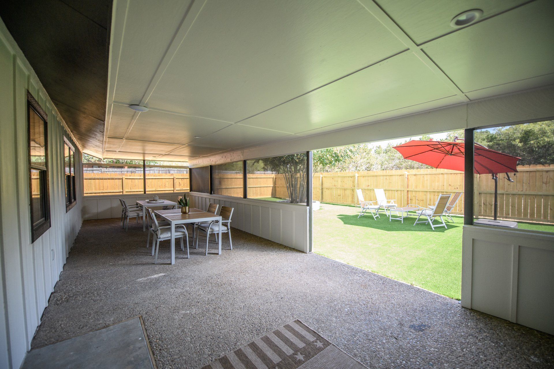 A screened in porch with tables and chairs and a red umbrella.