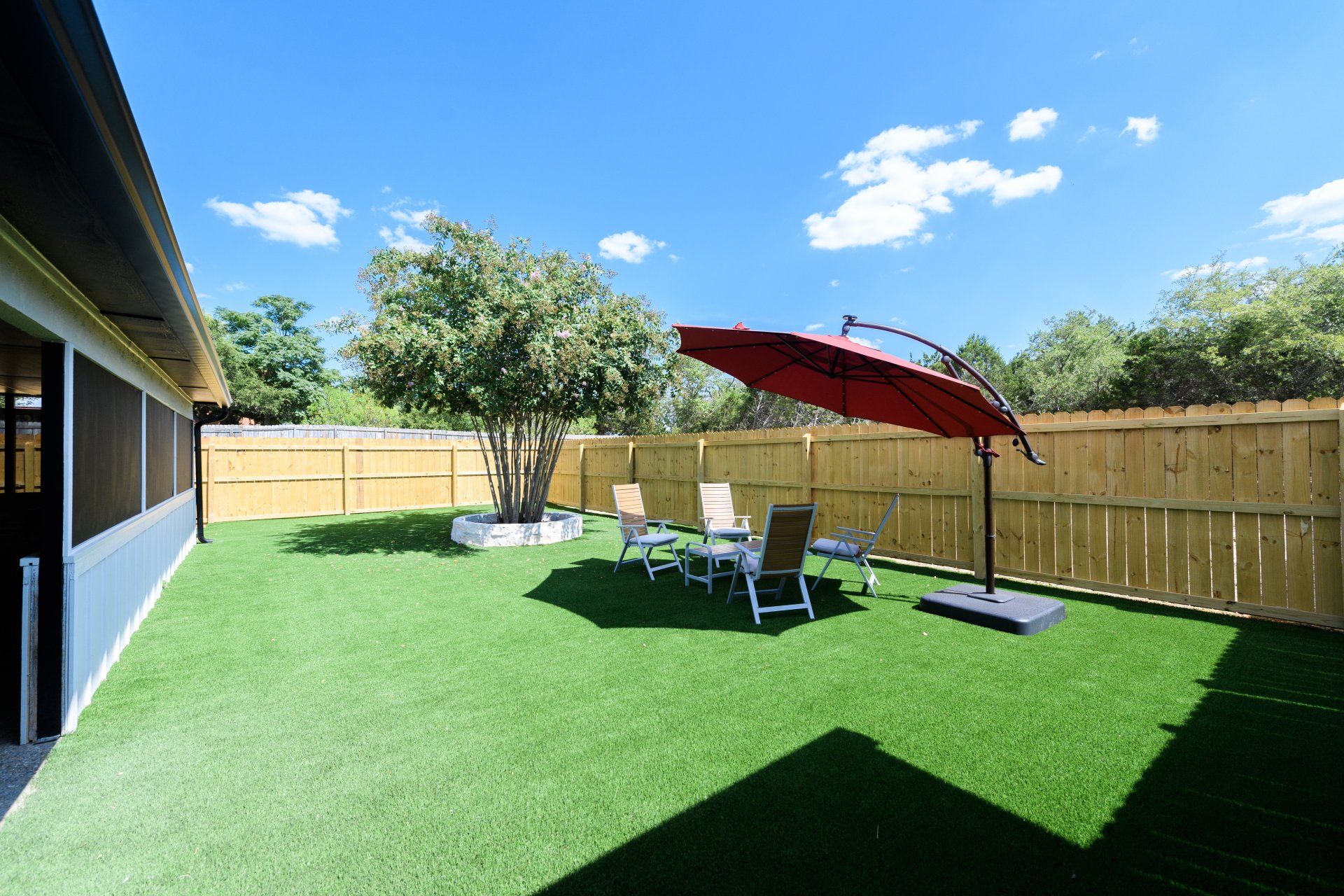A backyard with a red umbrella , chairs , and a wooden fence.