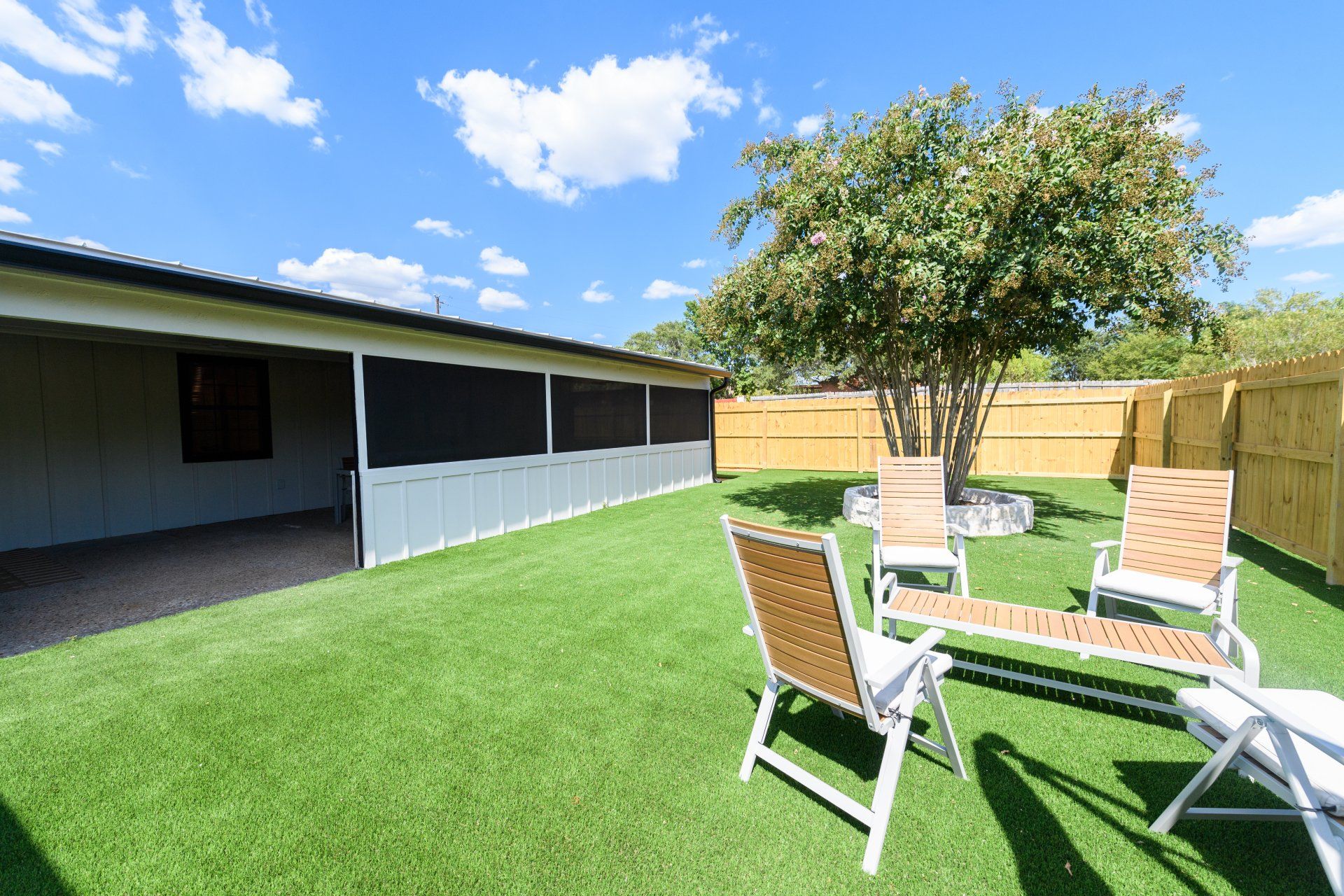 A backyard with lawn chairs and a table under a tree