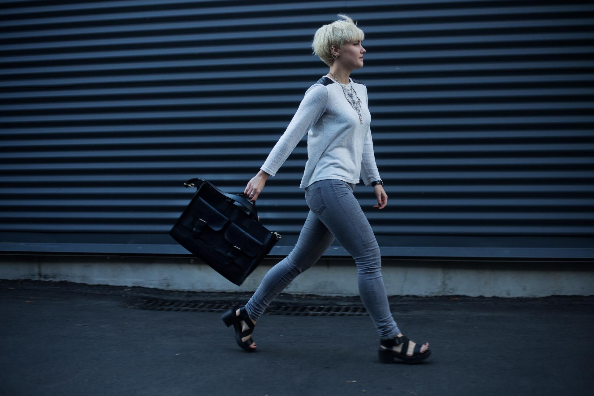 A woman is walking down the street carrying a black briefcase.