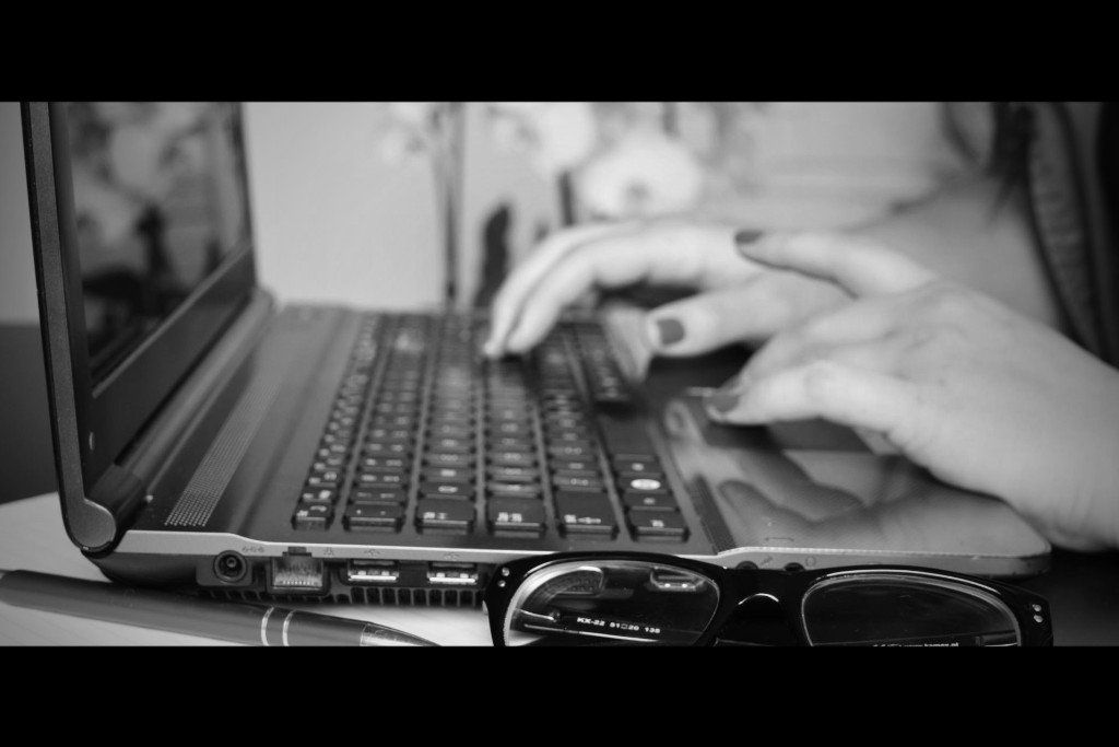 A black and white photo of a person typing on a laptop