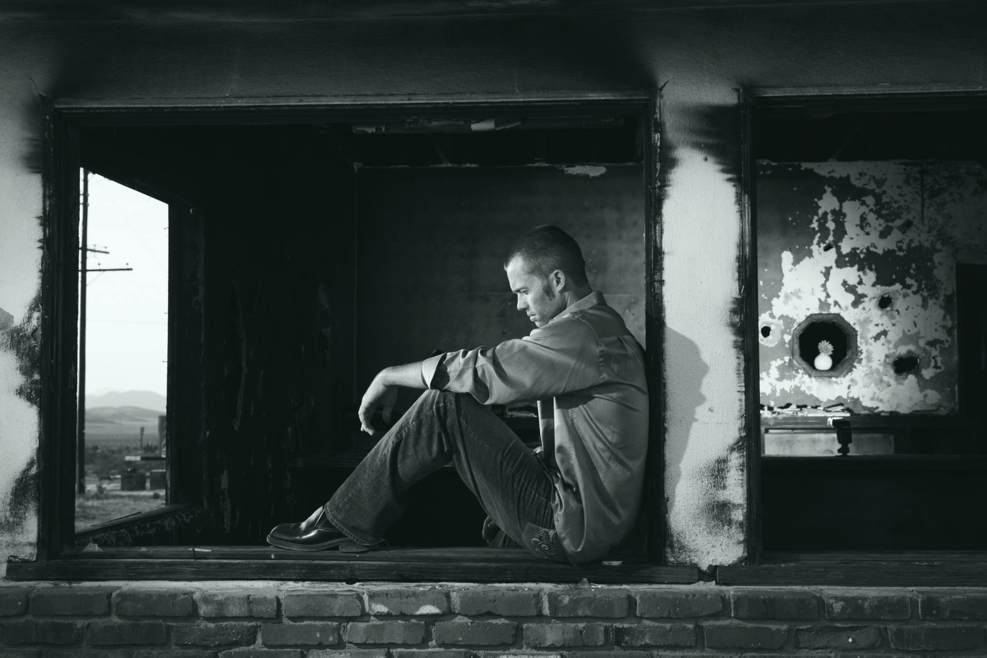A man is sitting on a window sill in a black and white photo.