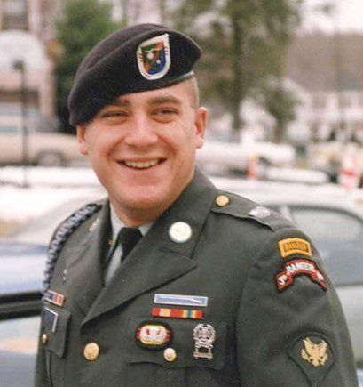 A man in a military uniform is smiling and wearing a black beret