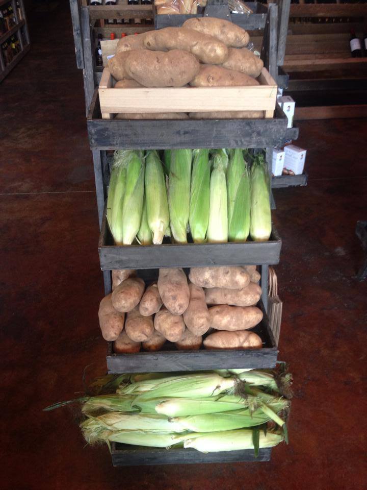 There are many different types of potatoes and corn on the cob on the shelves.