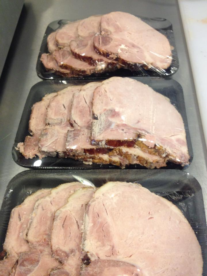 Three trays of sliced ham are sitting on a counter.