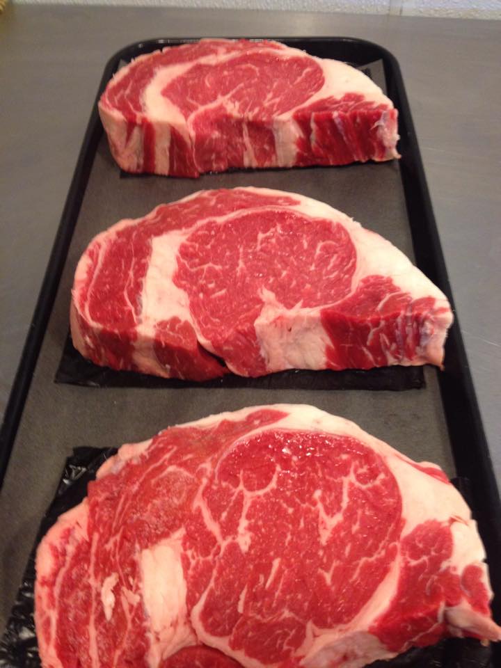 Three raw steaks are lined up on a tray