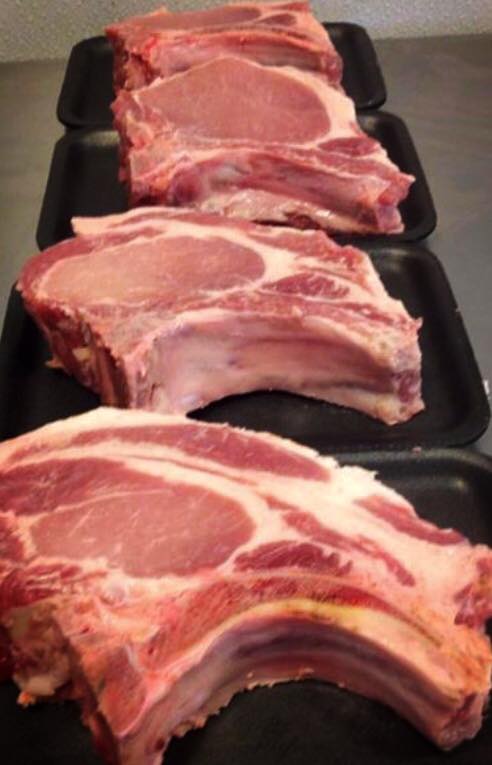 Three trays of raw pork chops are lined up on a counter.