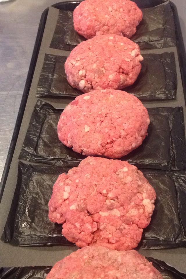 Four raw hamburger patties are lined up on a tray