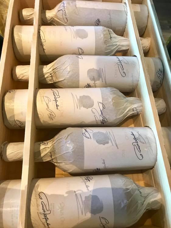 A wooden shelf filled with bottles of wine wrapped in paper.