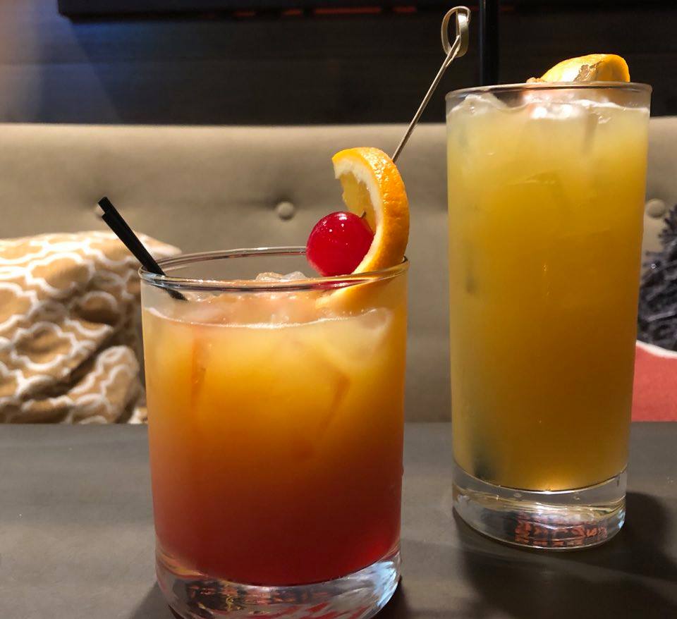 Two drinks are on a table with a couch in the background