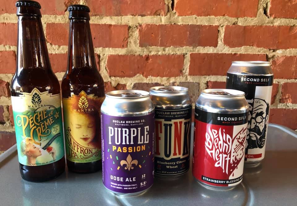 Bottles and cans of beer are lined up on a table in front of a brick wall.