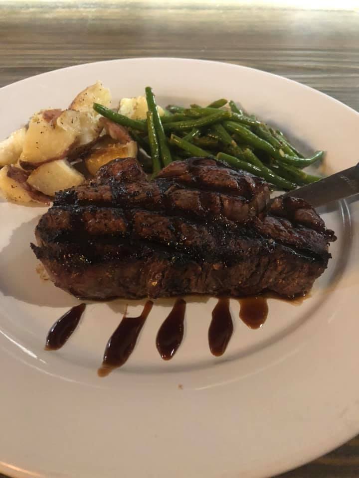 A white plate topped with a steak , green beans and potatoes.