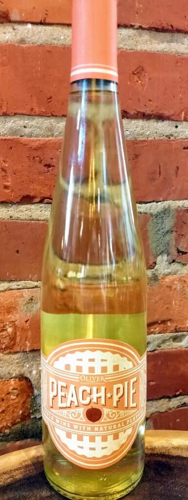 A bottle of peach pie is sitting in front of a brick wall.