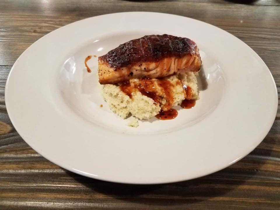 A white plate topped with a piece of meat and mashed potatoes